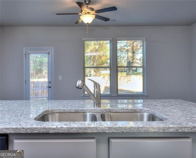 kitchen with ceiling fan, light stone countertops, and sink