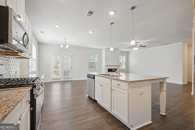 kitchen featuring an island with sink, ceiling fan with notable chandelier, appliances with stainless steel finishes, and white cabinetry