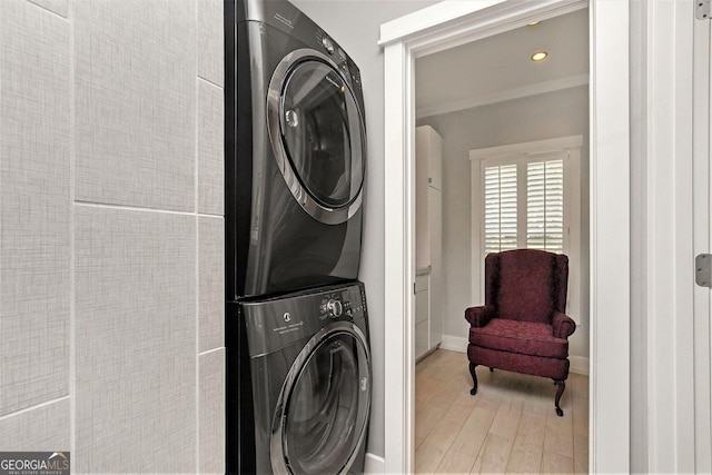 clothes washing area featuring stacked washing maching and dryer, light hardwood / wood-style flooring, and crown molding