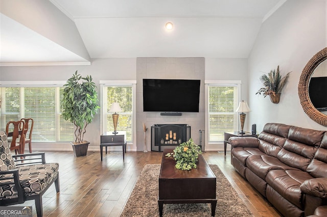 living room featuring wood-type flooring, a tiled fireplace, and vaulted ceiling