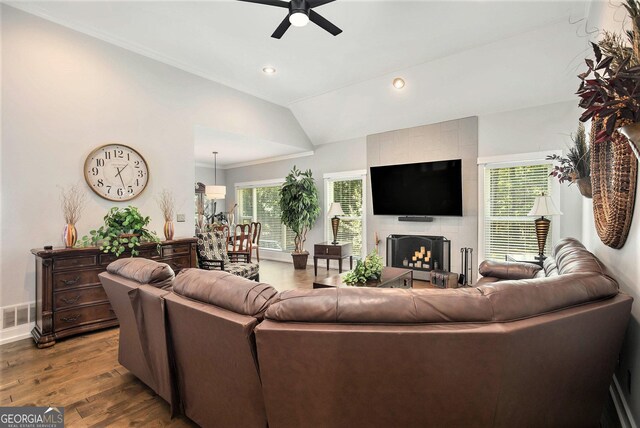 living room with wood-type flooring, ornamental molding, vaulted ceiling, ceiling fan, and a tile fireplace