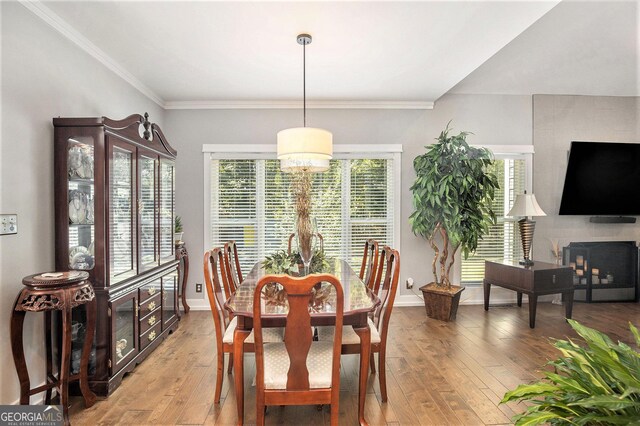 dining area with wood-type flooring, a large fireplace, and crown molding