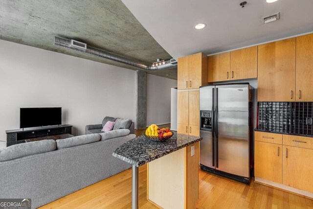 kitchen featuring a breakfast bar, dark stone countertops, light wood-type flooring, and stainless steel fridge with ice dispenser