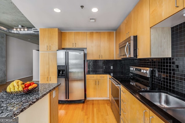 kitchen featuring backsplash, light wood-type flooring, stainless steel appliances, sink, and dark stone counters