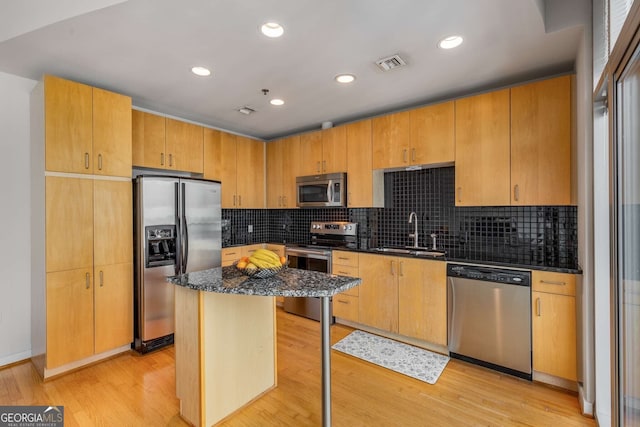 kitchen featuring a kitchen island, appliances with stainless steel finishes, sink, light wood-type flooring, and dark stone counters