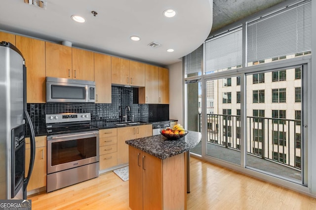 kitchen featuring light wood-type flooring, a kitchen island, sink, decorative backsplash, and appliances with stainless steel finishes