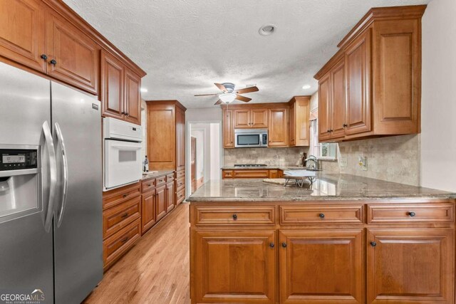 5775 Lakeshore Dr, Buford, GA 30518 - kitchen featuring appliances with stainless steel finishes, light wood-type flooring, brown cabinetry, a ceiling fan, and a sink