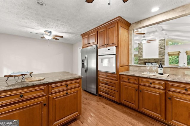 kitchen featuring oven, light hardwood / wood-style flooring, stainless steel fridge, ceiling fan, and vaulted ceiling with beams