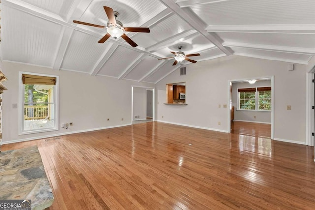 unfurnished living room featuring plenty of natural light, wood-type flooring, ceiling fan, and vaulted ceiling with beams