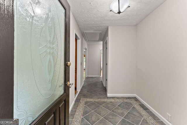 5775 Lakeshore Dr, Buford, GA 30518 - hallway featuring inlaid floor details, baseboards, dark tile patterned flooring, a textured ceiling, and attic access