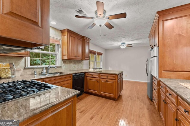 kitchen featuring light hardwood / wood-style floors, sink, black dishwasher, ceiling fan, and a textured ceiling