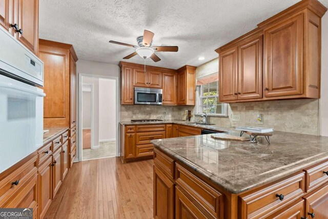 kitchen with a textured ceiling, backsplash, sink, ceiling fan, and light wood-type flooring