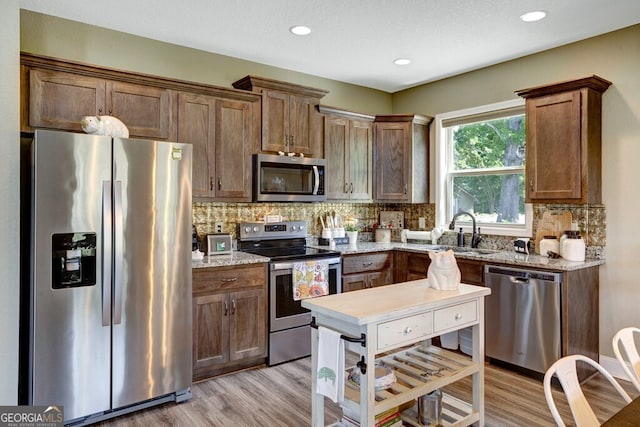 kitchen with appliances with stainless steel finishes, light stone counters, backsplash, and sink