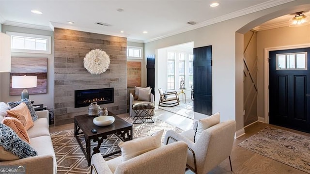 living room with a tile fireplace, plenty of natural light, and crown molding