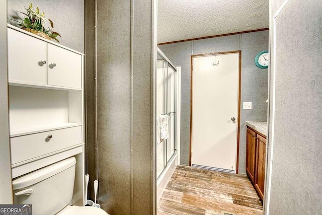 bathroom with toilet, walk in shower, hardwood / wood-style floors, crown molding, and vanity