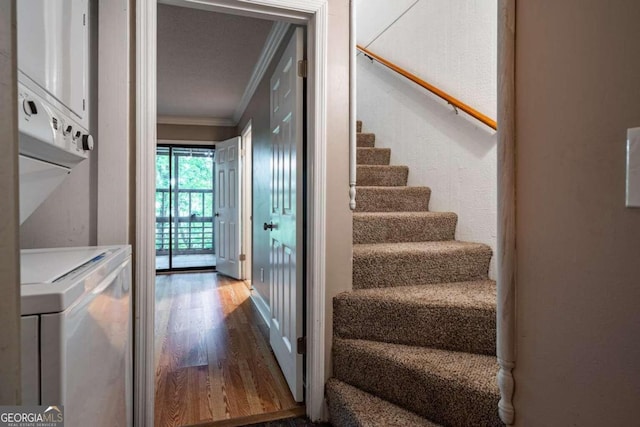 stairs with crown molding, a textured ceiling, wood-type flooring, and stacked washing maching and dryer