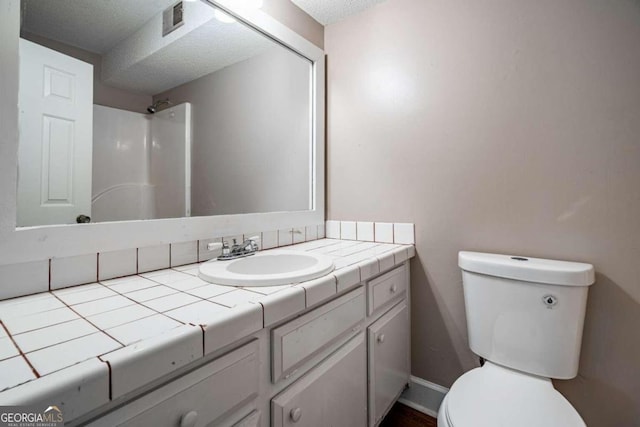 bathroom featuring a textured ceiling, vanity, toilet, and walk in shower