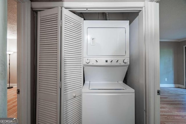 laundry room featuring a textured ceiling, crown molding, hardwood / wood-style floors, and stacked washer and dryer