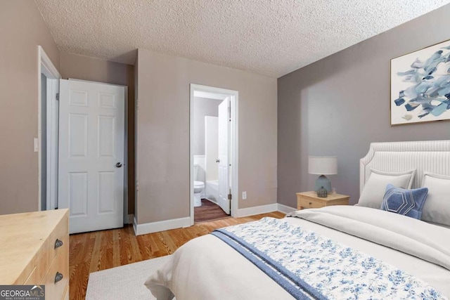 bedroom with a textured ceiling, connected bathroom, and light hardwood / wood-style floors