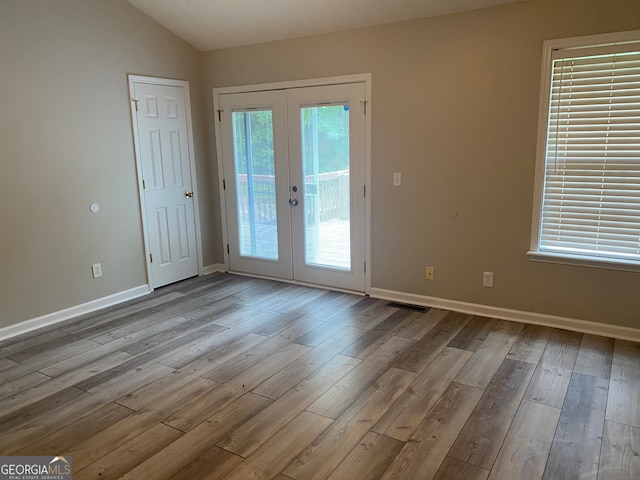 doorway to outside with a wealth of natural light, vaulted ceiling, light wood-type flooring, and french doors