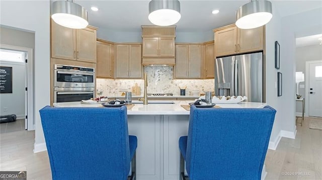 kitchen featuring hanging light fixtures, stainless steel appliances, a center island with sink, and light hardwood / wood-style flooring