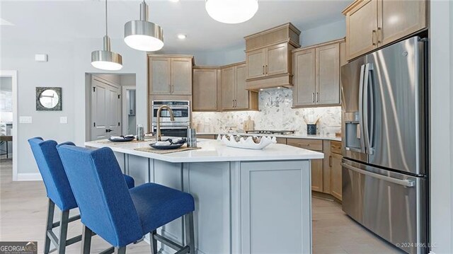 kitchen featuring an island with sink, hanging light fixtures, stainless steel appliances, decorative backsplash, and light wood-type flooring