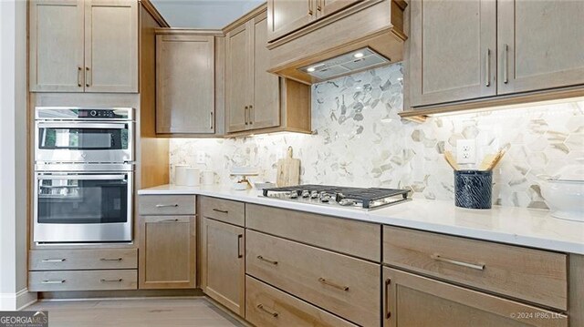 kitchen featuring light hardwood / wood-style flooring, light stone countertops, stainless steel appliances, premium range hood, and tasteful backsplash