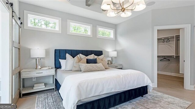 bedroom featuring an inviting chandelier, light hardwood / wood-style flooring, a barn door, a closet, and a walk in closet