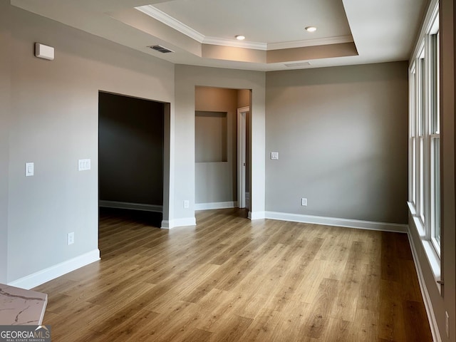 empty room with visible vents, light wood-style flooring, baseboards, and a tray ceiling