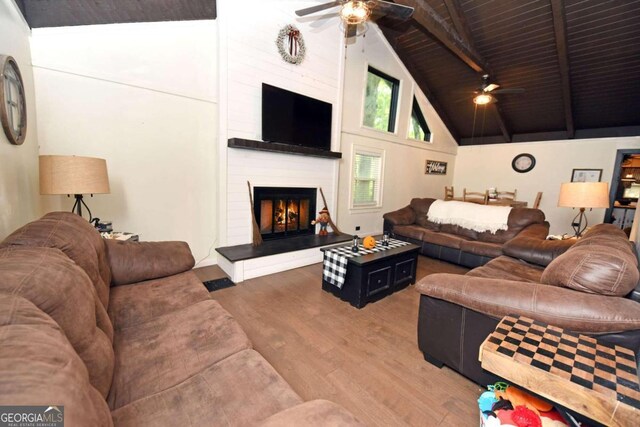 living room with hardwood / wood-style flooring, wooden ceiling, a large fireplace, beamed ceiling, and ceiling fan