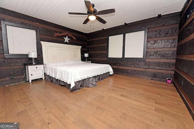 bedroom featuring a barn door, wood walls, ceiling fan, and light hardwood / wood-style floors