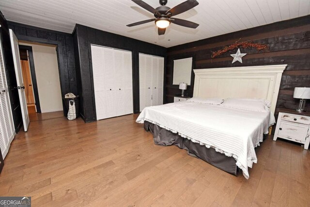 bedroom with two closets, wooden ceiling, wood-type flooring, wood walls, and ceiling fan