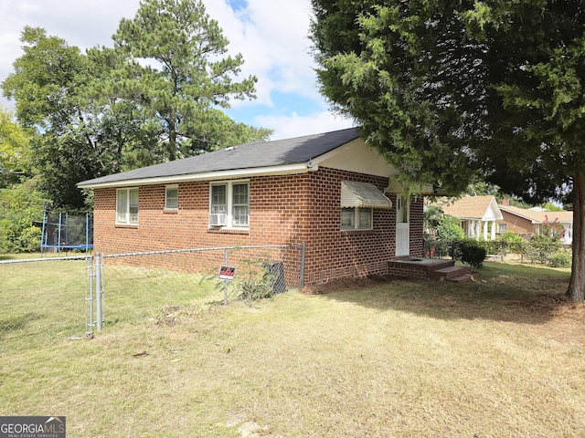 view of home's exterior featuring brick siding, a trampoline, fence, a lawn, and cooling unit