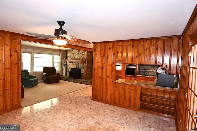 interior space featuring wall oven, a fireplace, crown molding, ceiling fan, and wooden walls