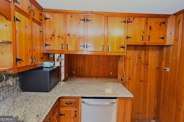 kitchen featuring stainless steel dishwasher, light stone countertops, wooden walls, and decorative backsplash