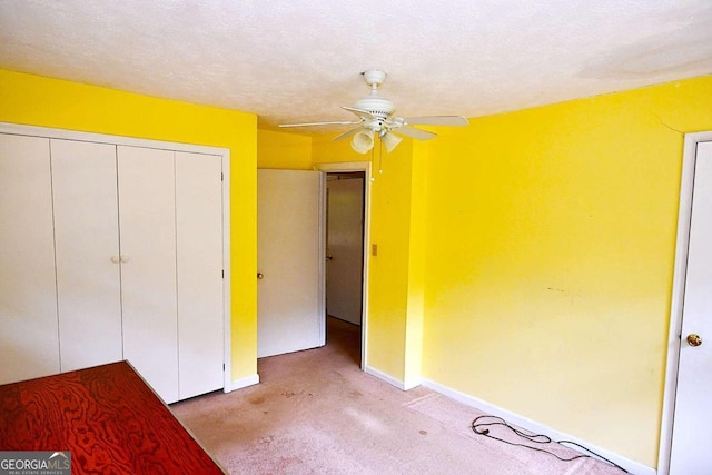 unfurnished bedroom with light carpet, a textured ceiling, ceiling fan, and a closet