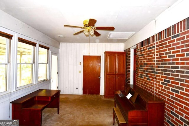 sitting room featuring ceiling fan, carpet floors, and brick wall