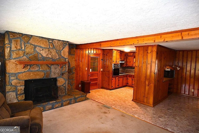 carpeted living room with a textured ceiling, wooden walls, and a stone fireplace