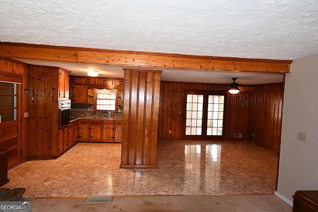 kitchen featuring a textured ceiling, wood walls, sink, ceiling fan, and french doors