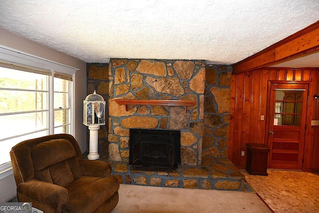 carpeted living room with a textured ceiling, wood walls, and a stone fireplace