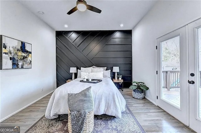 bedroom with light hardwood / wood-style floors, ceiling fan, wood walls, and access to exterior