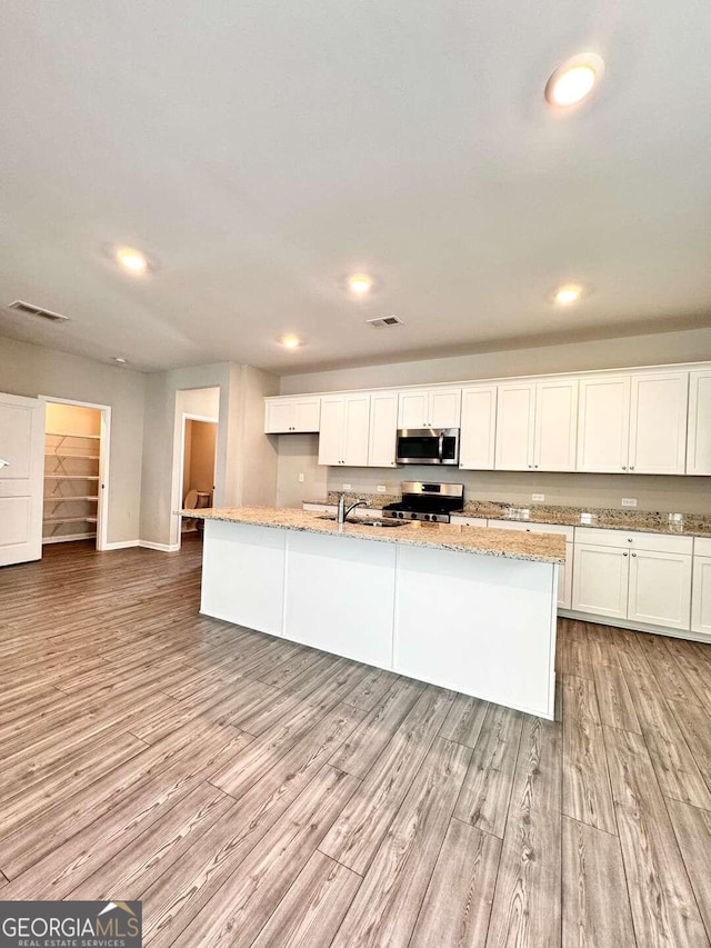 kitchen with light wood-type flooring, stainless steel appliances, white cabinets, and a center island with sink