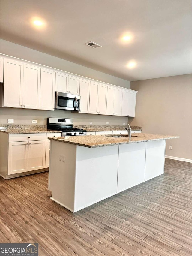 kitchen featuring light wood-type flooring, stainless steel appliances, white cabinets, and a center island with sink