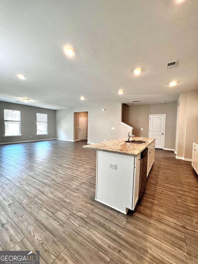 kitchen featuring white cabinets, hardwood / wood-style floors, light stone countertops, black dishwasher, and a center island with sink