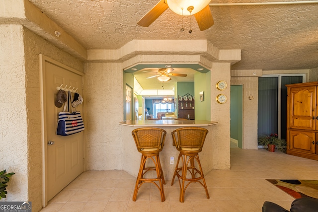 kitchen featuring a kitchen breakfast bar, a textured ceiling, kitchen peninsula, and light tile patterned floors