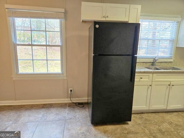 kitchen with light stone counters, a wealth of natural light, black refrigerator, white cabinetry, and sink