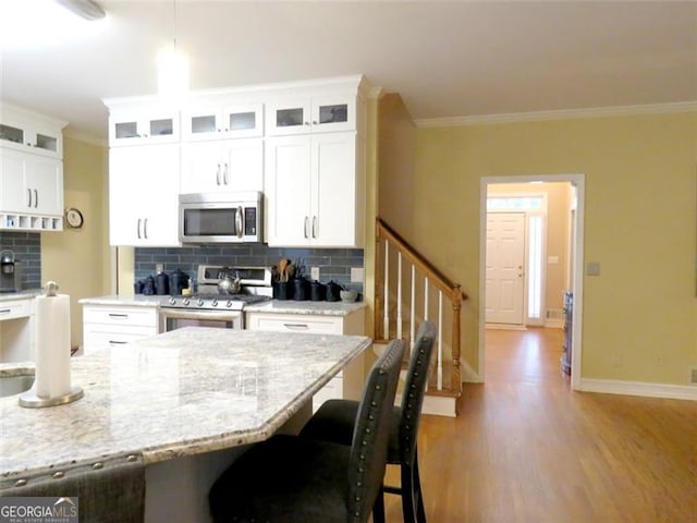 kitchen featuring ornamental molding, light hardwood / wood-style floors, stainless steel appliances, white cabinets, and decorative backsplash