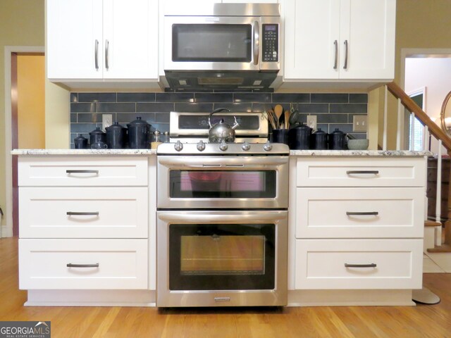 kitchen with white cabinetry, backsplash, stainless steel appliances, and light stone counters