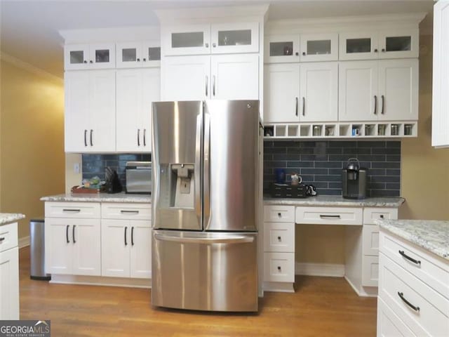 kitchen with light stone countertops, light wood-type flooring, backsplash, white cabinets, and stainless steel refrigerator with ice dispenser