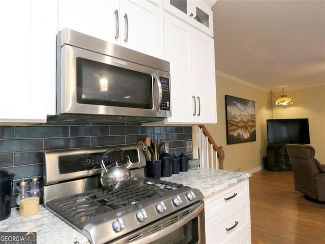 kitchen with appliances with stainless steel finishes, backsplash, white cabinetry, light stone counters, and hardwood / wood-style flooring